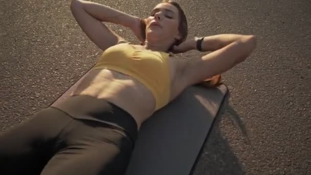 Una buena mujer delgada en ropa deportiva haciendo crujidos en la alfombra de fitness al aire libre
 - Imágenes, Vídeo