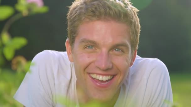MOCIÓN LENTA: El hombre feliz sonríe y mira a la cámara mientras está acostado en la hierba
 - Metraje, vídeo