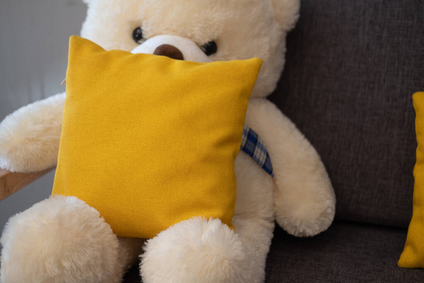 Yellow pillow and teddy bear on sofa in living room - Zdjęcie, obraz