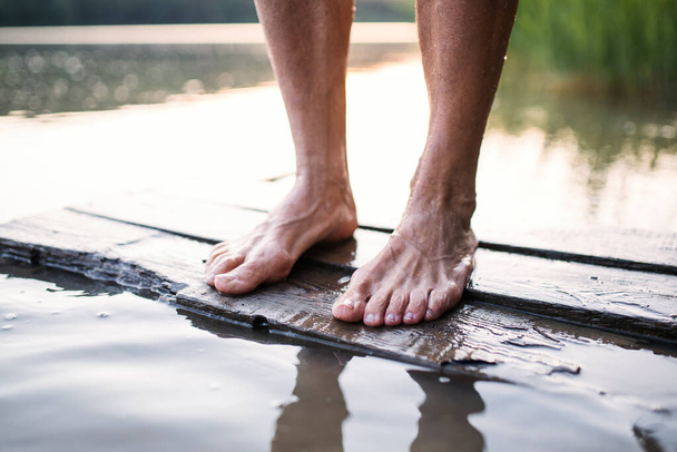 Bare feet of woman standing by lake outdoors before swimming. - Photo, image