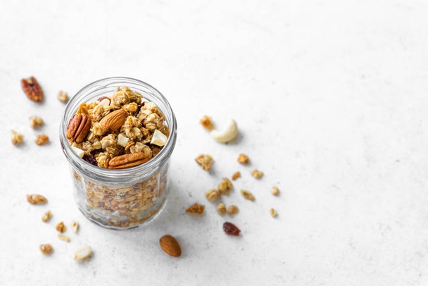 Organic granola with nuts and seeds in glass jar. Homemade Granola for healthy breakfast on white, copy space. - Фото, изображение