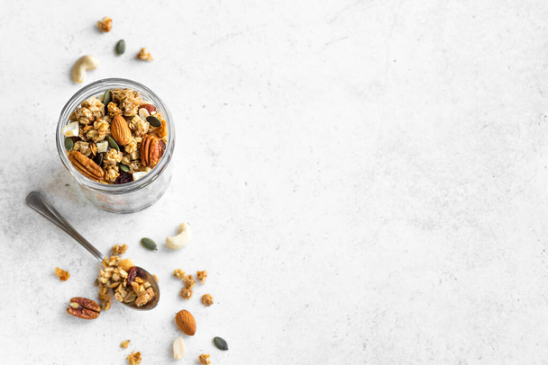Homemade granola with nuts and seeds in glass jar. Granola for healthy breakfast on white, top view, copy space. - Φωτογραφία, εικόνα