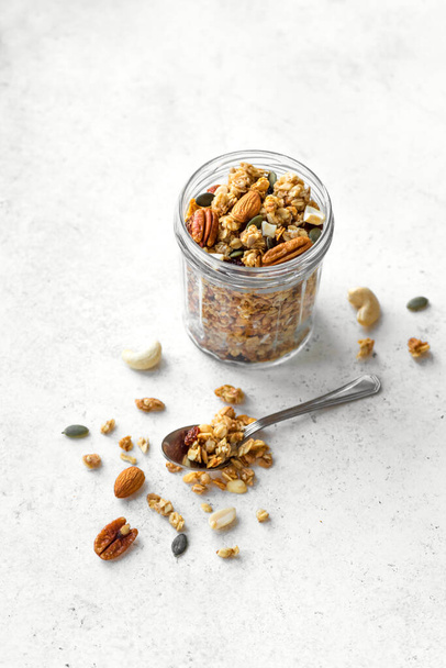 Homemade granola with nuts and seeds in glass jar. Granola for healthy breakfast on white, copy space. - Foto, afbeelding