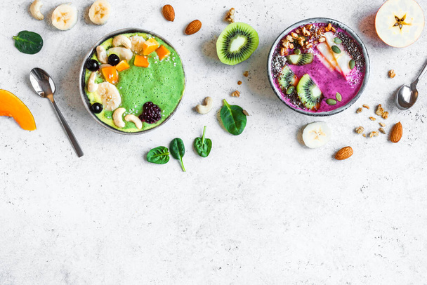 Kleurrijke Smoothie Bowls voor gezond detox ontbijt, bovenaanzicht, kopieerruimte. Groene spinazie en bessen smoothie kommen met verschillende toppings. Veganistisch rauw voedsel, gezond eten concept. - Foto, afbeelding