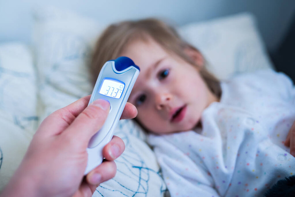 Imagen del padre midiendo la temperatura de la niña con termómetro infrarrojo en casa. Concepto de gripe
 - Foto, imagen