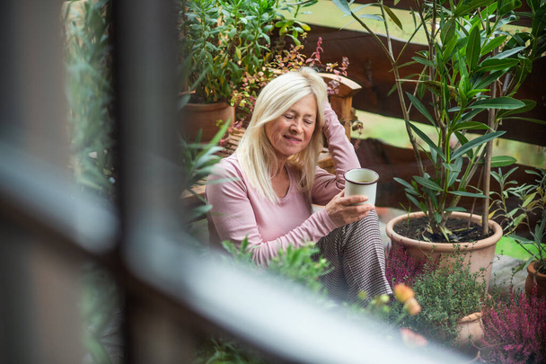 Senior woman with coffee sitting outdoors on terrace, resting. - Φωτογραφία, εικόνα
