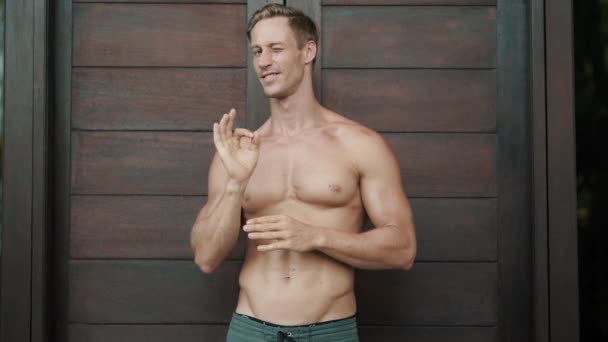 positive guy shows OK sign and winks at stylish wooden door - Footage, Video