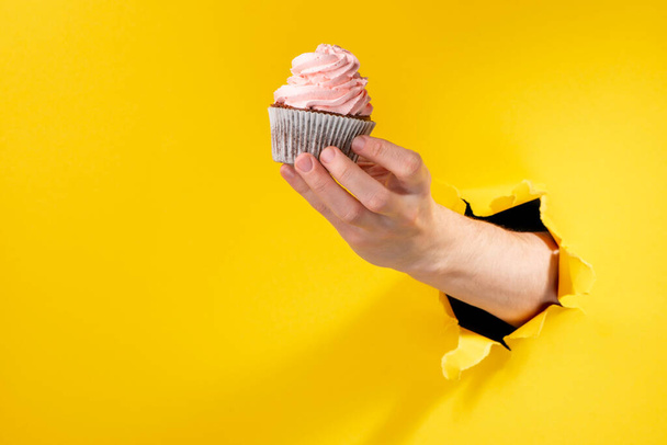 Hand holding a cupcake with pink buttercream swirl - Fotoğraf, Görsel