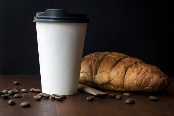 Caffè da portare in una tazza di carta con croissant su un tavolo di legno. - Foto, immagini