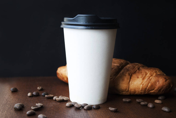 Café para ir em uma xícara de papel com croissants em uma mesa de madeira. - Foto, Imagem