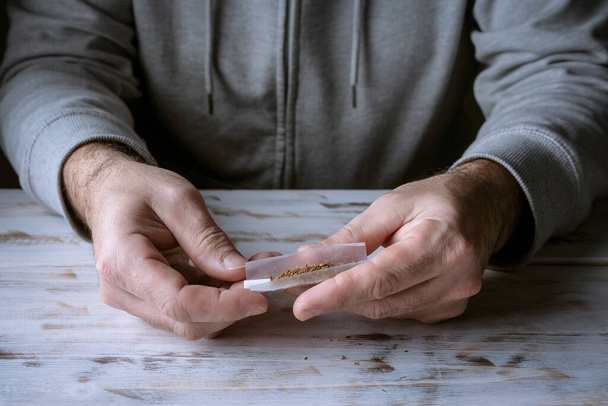 Mann dreht eine Marihuana-Zigarre mit seinen eigenen Händen auf einem Holztisch, Raucherkonzept - Foto, Bild