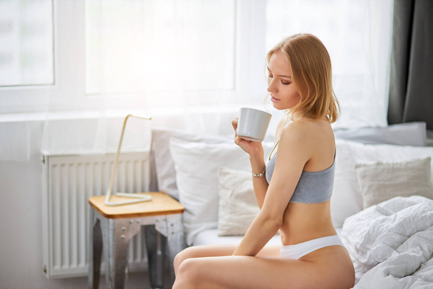 sweet pretty woman in underwear drink hot coffee or tea on bed - Φωτογραφία, εικόνα