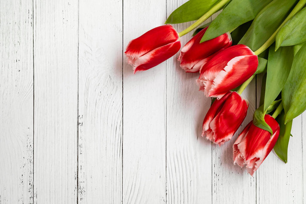 A bouquet of five bright, red tulips with a white carved border lie on a white wooden table. - 写真・画像
