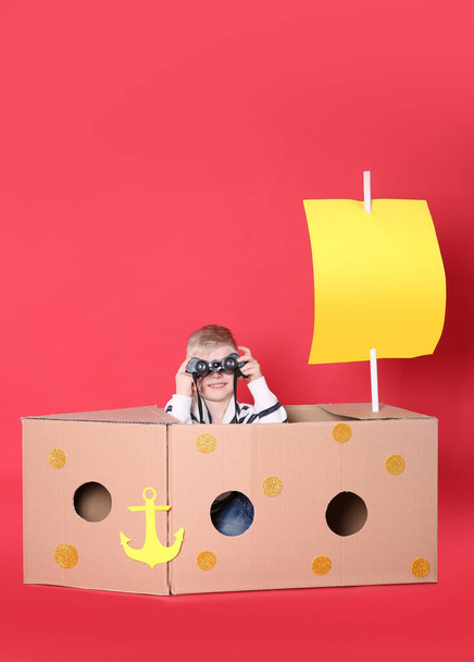 Little child playing with ship made of cardboard box on red background - Fotoğraf, Görsel