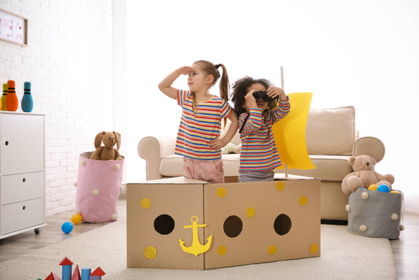 Cute little children playing with cardboard ship and binoculars at home - Foto, Imagem