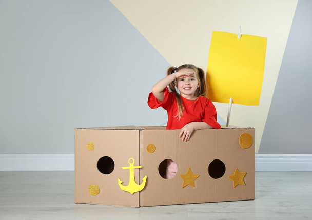 Cute little child playing with cardboard ship near color wall - Zdjęcie, obraz