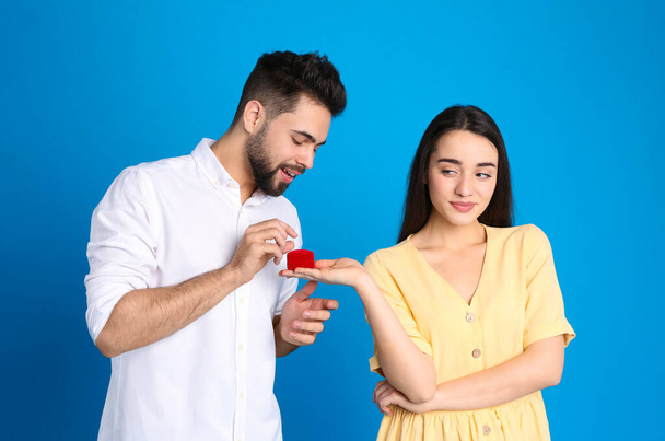 Young woman with engagement ring making marriage proposal of marriage to her boyfriend on blue background - 写真・画像