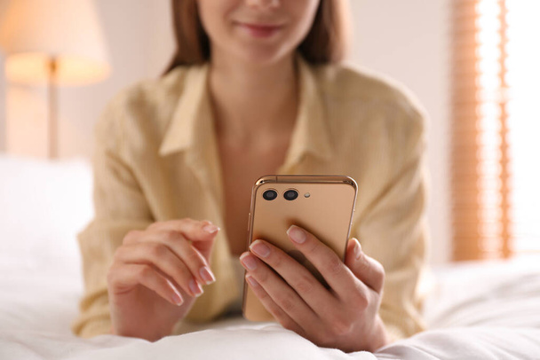 Young woman using modern smartphone on bed at home, closeup - Fotoğraf, Görsel