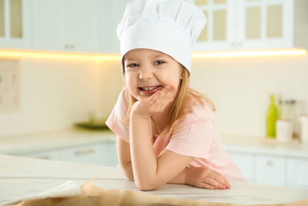 Portrait of cute little girl wearing chef hat in kitchen - Fotografie, Obrázek