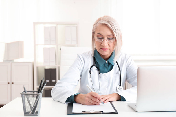 Mature female doctor working at table in office - Photo, image