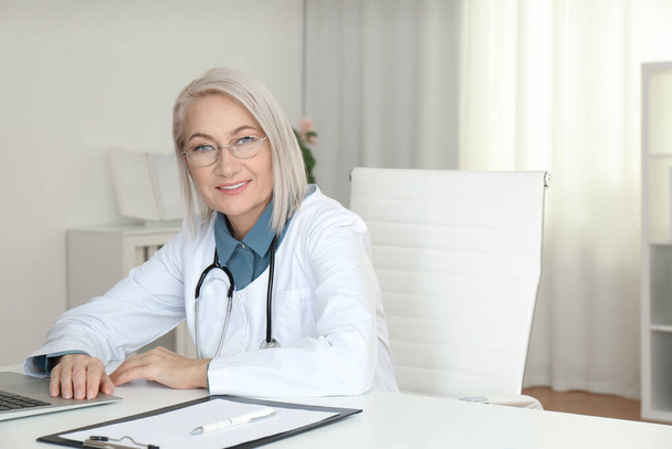 Portrait of mature female doctor in white coat at workplace - Fotografie, Obrázek