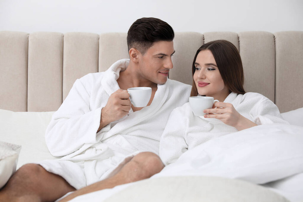 Happy couple in bathrobes with coffee on bed at home - Foto, Imagem