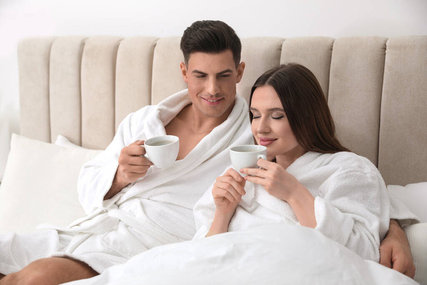 Happy couple in bathrobes with coffee on bed at home - Фото, зображення