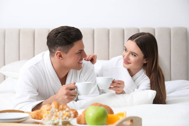 Happy couple in bathrobes with coffee on bed at home - Foto, Bild