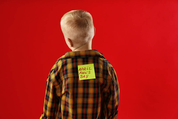 Little boy with APRIL FOOL'S DAY sticker on back against red background - Zdjęcie, obraz