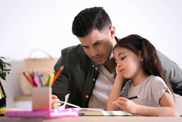 Man helping his daughter with homework at table indoors - Фото, изображение