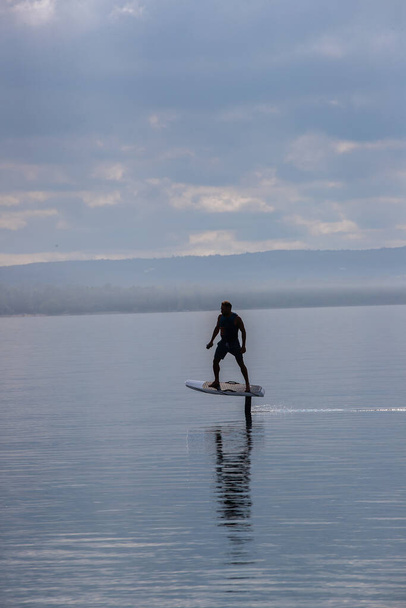 Человек на электрической доске из фольги на озере в спасательном жилете
 - Фото, изображение
