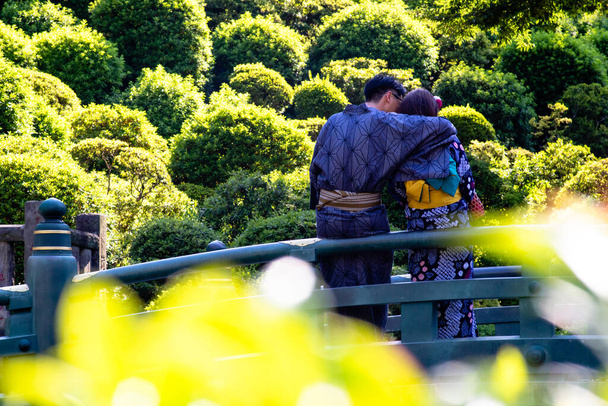A young couple wearing kimonos cuddling on a bridge - Photo, Image