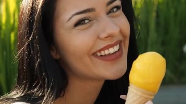Jonge schoonheidsvrouw eet ijs in Slow Motion Hd Video. Ze glimlacht en likt gele gelato voor bladeren van riet en oever van de rivier. Lage scherptediepte en wazige achtergrond. - Video