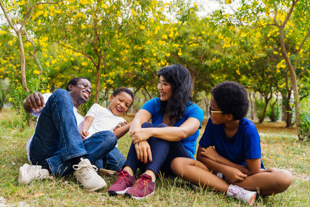 Feliz e saudável família afro-americana de quatro pendurados e sentados no parque verde
. - Foto, Imagem