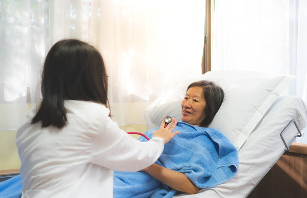Een arts die stethoscoop gebruikt om een oude Aziatische patiënt te onderzoeken op de afdeling van het ziekenhuis in de ochtend. - Foto, afbeelding
