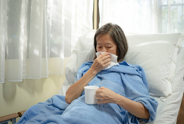 Vanha aasialainen nainen makaa sängyllä paitsi ikkunat flunssan takia
 - Valokuva, kuva
