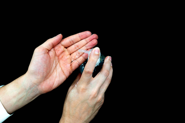 lewa ręka pompująca żel nasączony alkoholem do prawej ręki w celu czyszczenia i zapobiegania infekcji (czarne tło) - Zdjęcie, obraz