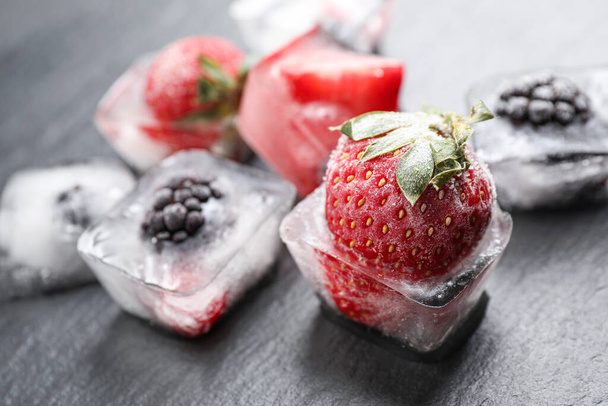 Ice cubes with different berries on dark grey table, closeup - 写真・画像