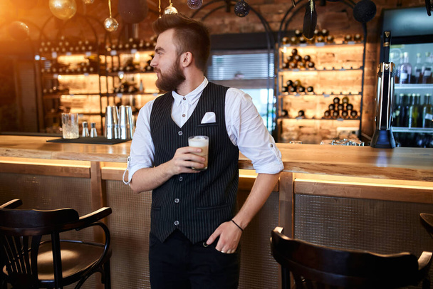 smiling cheerful barista holding a glass and looking aiside - Foto, immagini