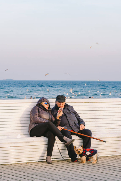 Polônia, Sopot, 9 de fevereiro de 2020. Casal sénior sentado no banco. Velho e mulher no banco perto do mar. O amor é tudo, o conceito de idade da aposentadoria e o amor. Marido e mulher idosos sentados juntos por mar
 - Foto, Imagem