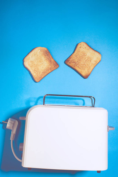 Leivänpaahdin viipaleilla leipää sinisellä pohjalla, tilaa tekstille. ylhäältä näkyvä pystysuora kuva. Litteä
 - Valokuva, kuva