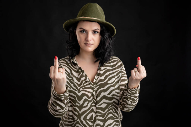 Молодая женщина, одетая в рубашку с изображением животного, с черными волосами в шляпе, изображающей двойной секс, который ты позируешь на черном изолированном заднем плане
. - Фото, изображение