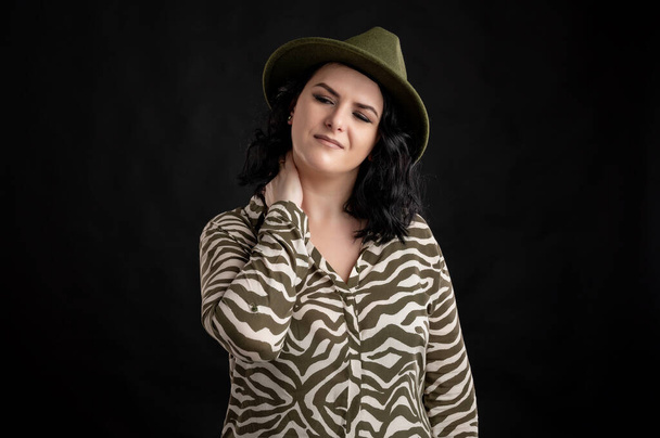 Young woman dressed casually in an animal print shirt, with black hair wearing a hat has sore throat posing on a black isolated backround. - Photo, Image