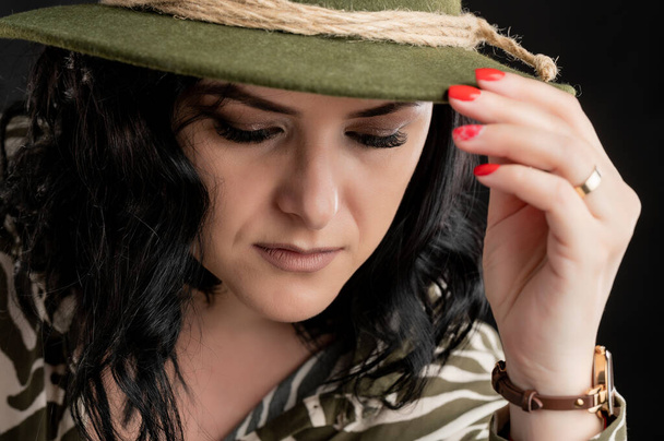 Young woman dressed casually in an animal print shirt, with black hair wearing a hat close-up portrait posing on a black isolated backround. - Foto, imagen