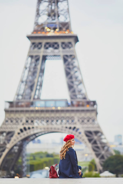 Young woman with long blond curly hair in Paris, France. Beautiful tourist in red beret near the Eiffel tower - Zdjęcie, obraz