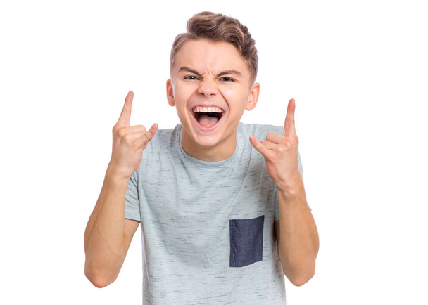 Portrait of teen boy making Rock Gesture, isolated on white background. Handsome caucasian young teenager showing horns up gesture. Happy cute child screams and doing heavy metal rock sign. - Photo, Image