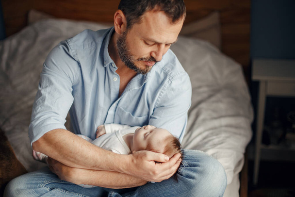 Λευκός πατέρας μεσήλικας με κοιμισμένο νεογέννητο κοριτσάκι. Γονιός κρατάει στα χέρια του τον γιο της κόρης του. Αυθεντική στιγμή πατρότητας. Οικογενειακή ζωή ανύπαντρων γονιών. - Φωτογραφία, εικόνα