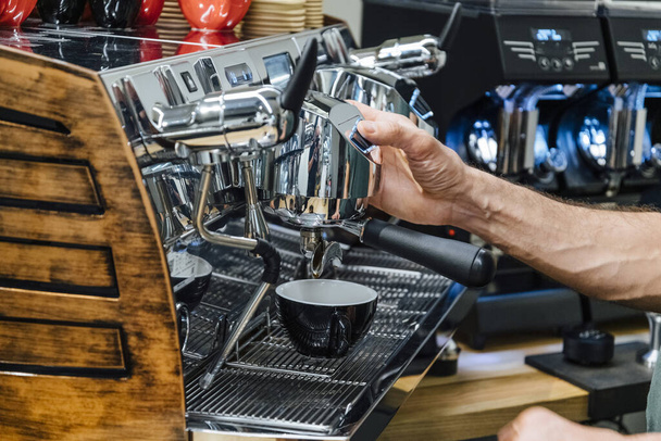 Primer plano de barista sosteniendo el soporte del filtro mientras la máquina de café prepara café recién exprés en vidrio - Foto, imagen
