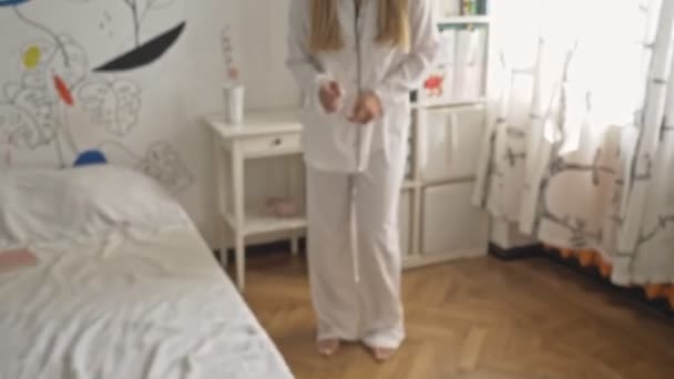 A pretty young woman wearing white pajamas is listening to music and dancing in the bedroom - Metraje, vídeo