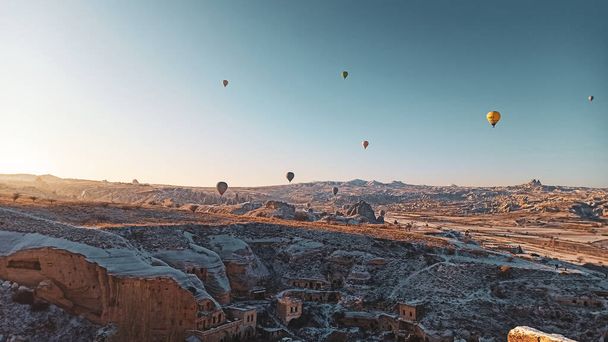 Colorful hot air balloons flying over the valley with fairy chimneys in winter season. Lots of Hot air balloons at the sunrise sky landscape in Cappadocia, Turkey - Фото, изображение